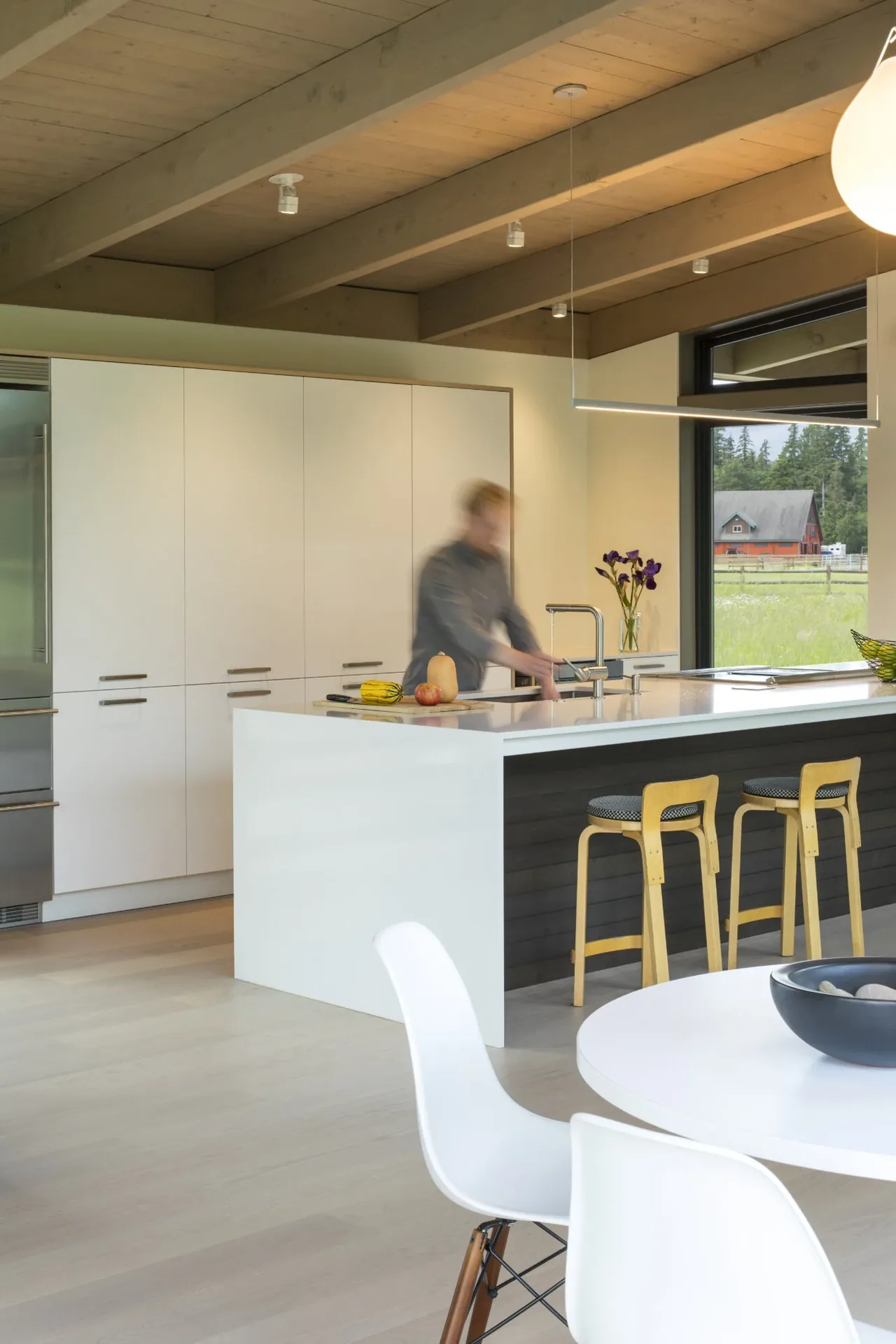 The Field House kitchen combines white cabinetry, wood beam ceiling, and large windows looking toward a rural view, by David Coleman Architecture.