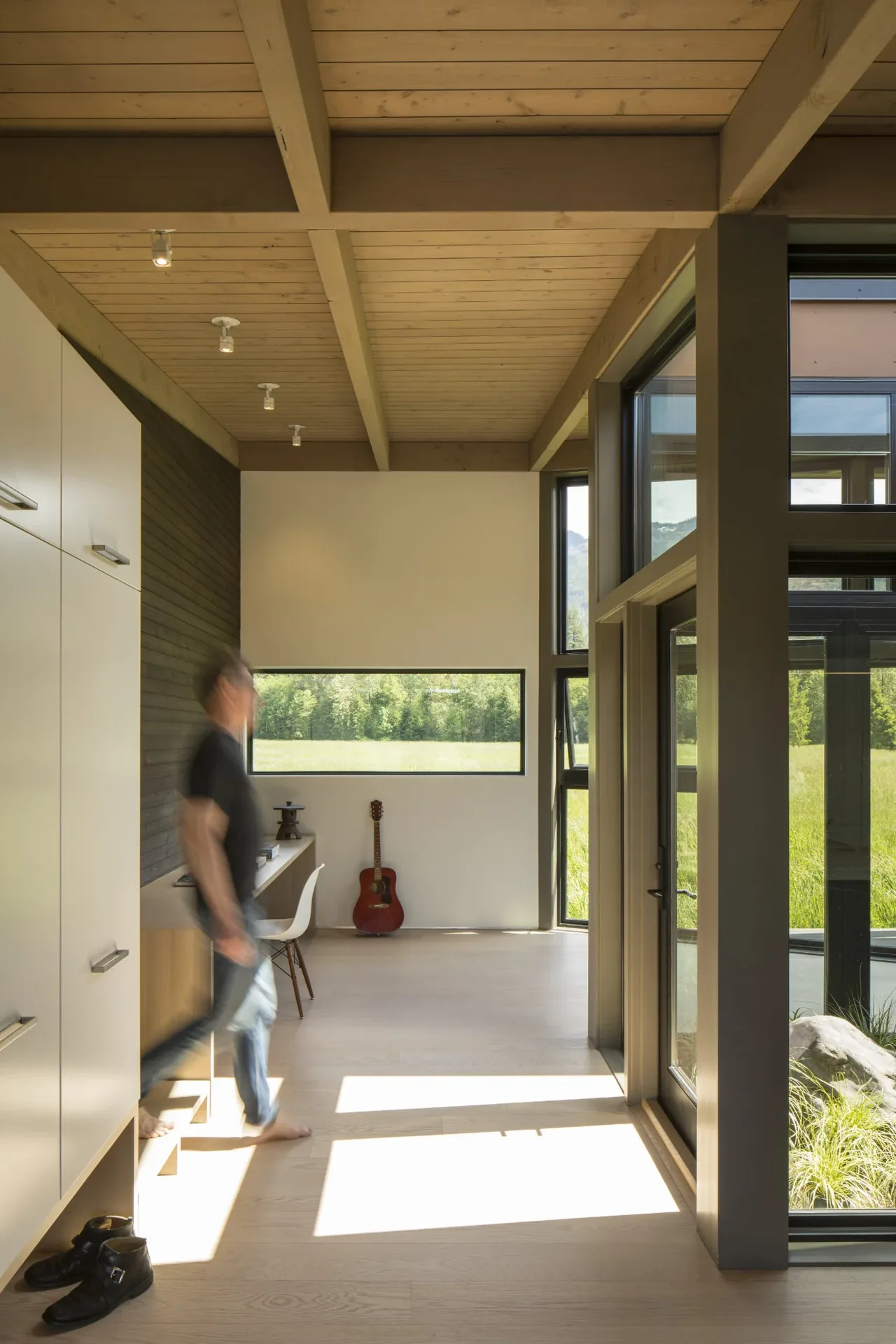 Hallway with exposed wood beam ceiling, light wood floors, and large windows overlooking the outdoor landscape.