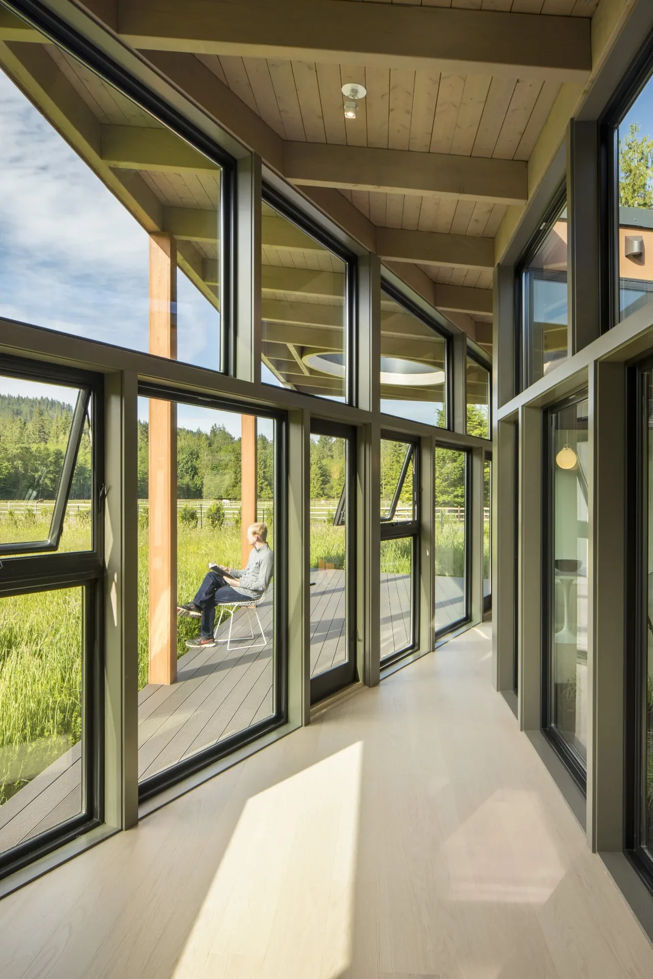 Field House interior hallway with floor-to-ceiling black window frames and wood beam ceiling overlooking the outdoor deck.