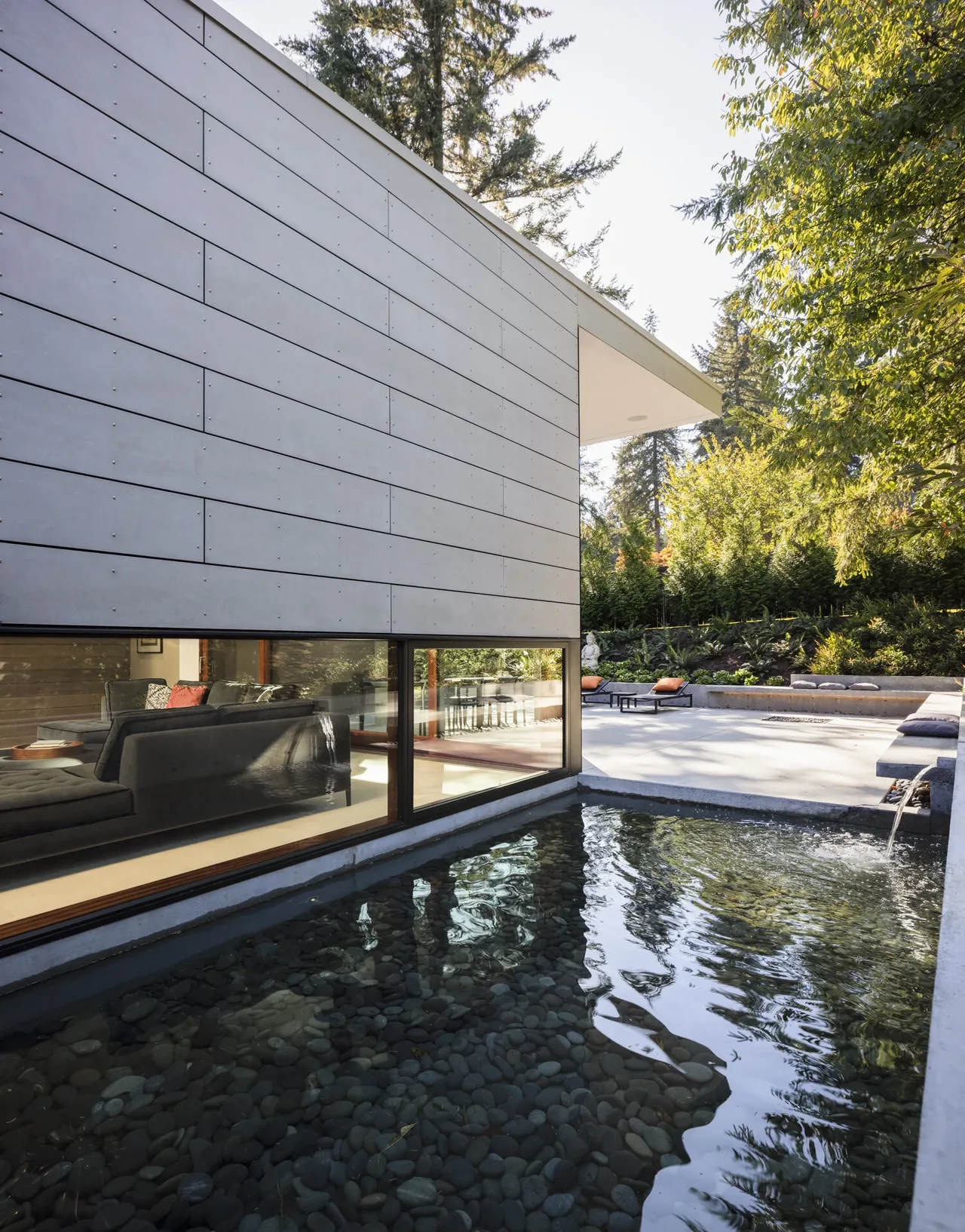 Modern exterior of Inside Outside House with a pebble base reflective water feature and landscaped outdoor seating area.
