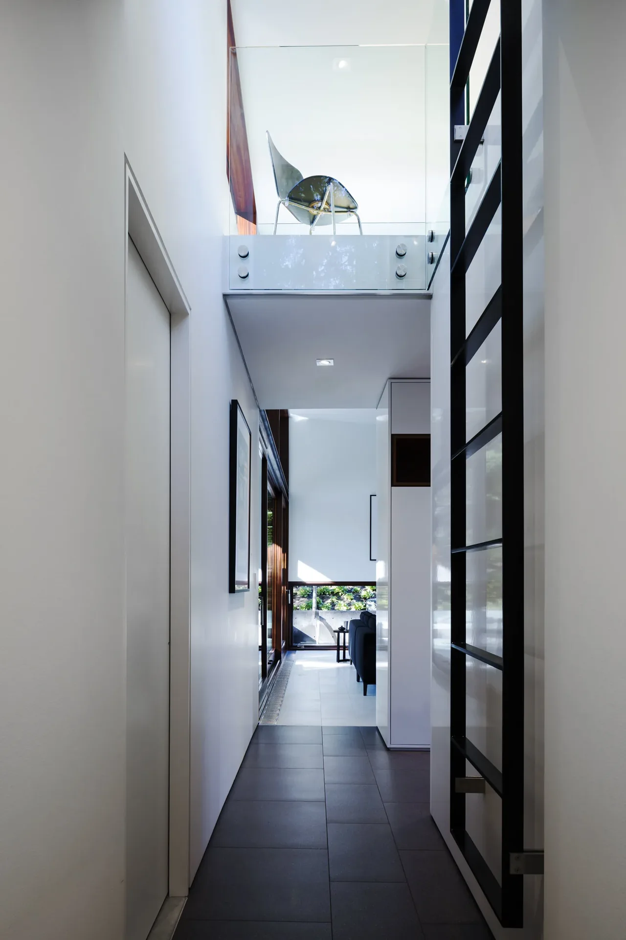 Interior hallway with black tiled floor, white walls, and glass-railed mezzanine overlooking the space