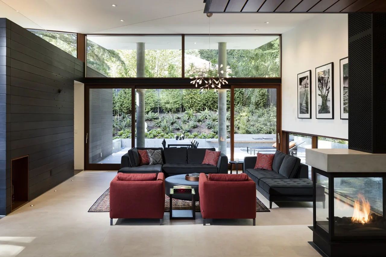 Living room with large glass doors opens to an outdoor patio with landscaping and dining furniture in the Seattle Inside Outside House.