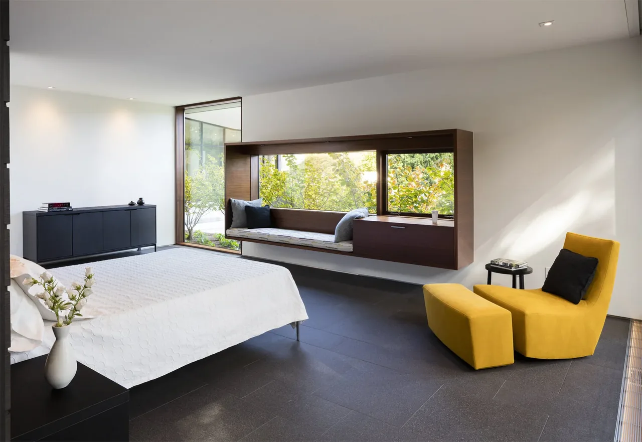Modern bedroom featuring a floating wood-framed window seat and a yellow lounge chair with ottoman.