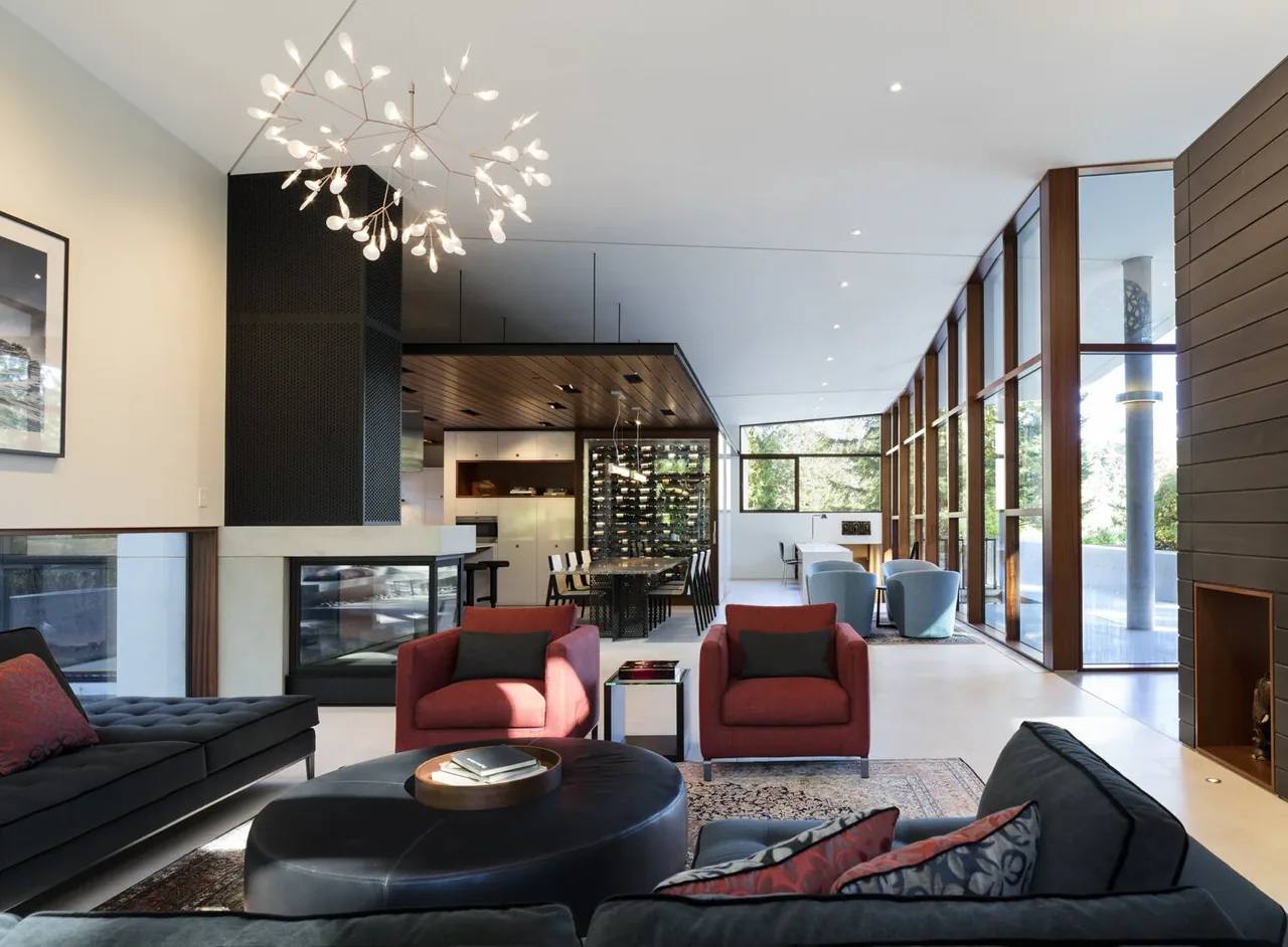 Inside Outside House features a spacious living and dining area with floor-to-ceiling wood-framed windows and a dual-sided fireplace.