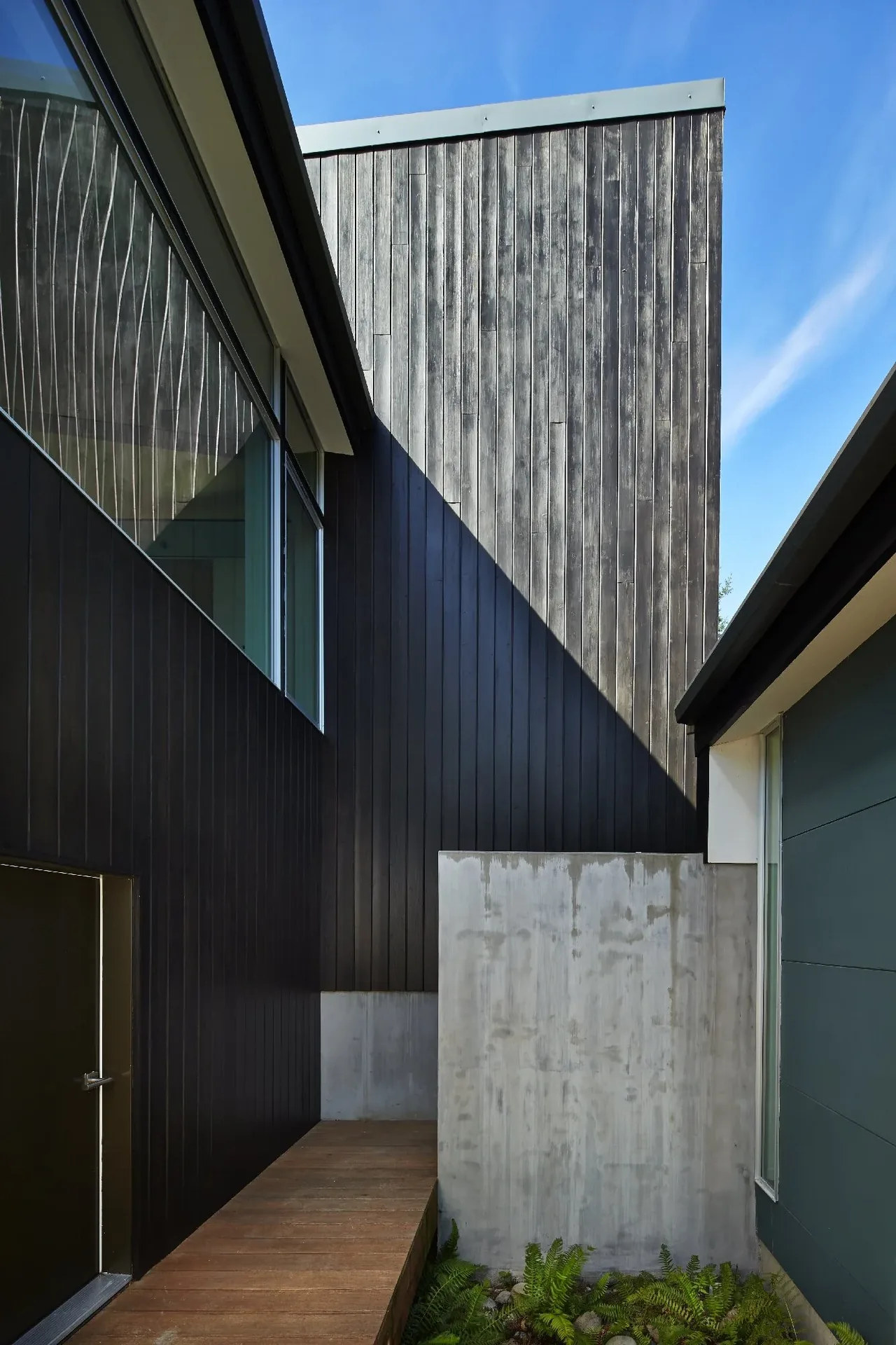Exterior passageway of Bear Run Cabin features dark wood siding and concrete walls under a clear blue sky.