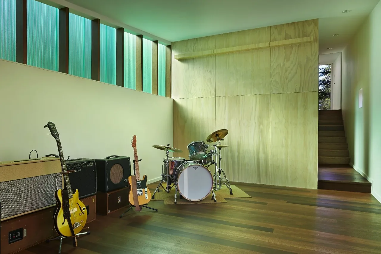 Music room featuring guitars, amplifiers, and a drum set with wood flooring and high clerestory windows.