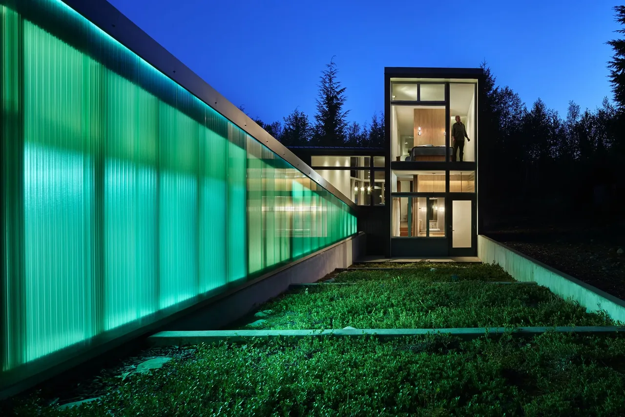 The Bear Run Cabin features a translucent green wall and large windows revealing its modern interior at night.