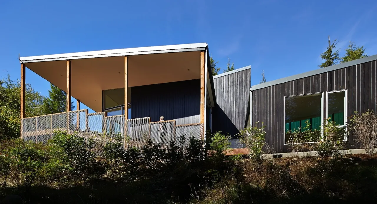 Bear Run Cabin features a flat roof and vertical wood siding with a glass and metal mesh railing on the raised deck.