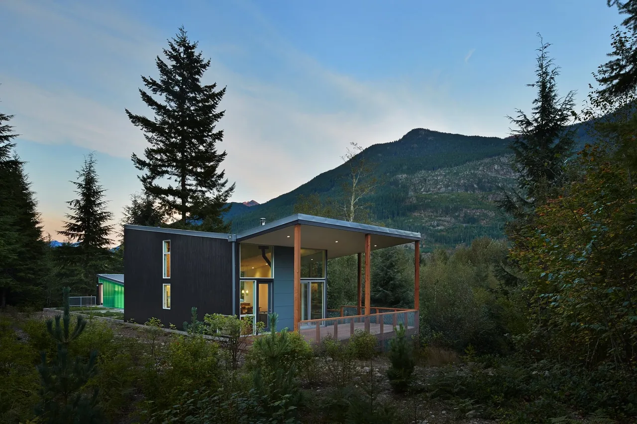 Bear Run Cabin by David Coleman Architecture features a flat roof and covered patio surrounded by forest and mountains.