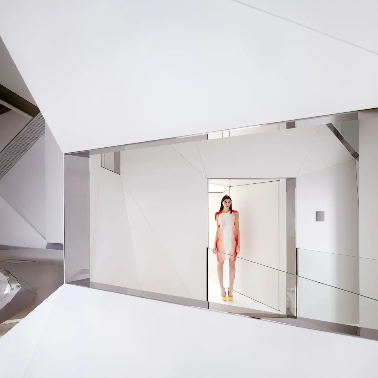 Interior view of a white minimalist space with geometric polished metal framing and glass railing.