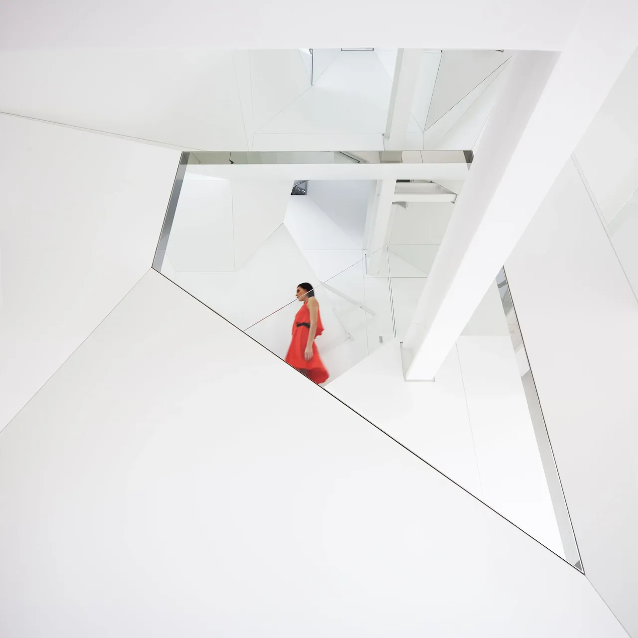 Woman in a red dress walking down a modern white staircase with glass railing inside a bright minimalist interior.