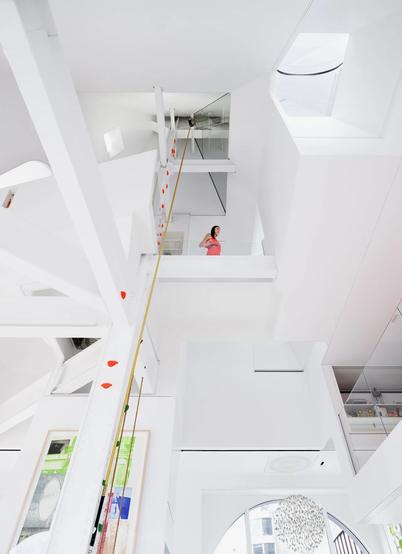 Multi-level modern minimalist interior with white walls, a climbing wall, and a person standing on a balcony.