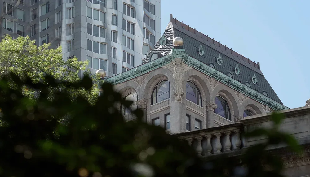 Historic building's ornate upper corner with rounded windows and green decorative cornice under blue sky.