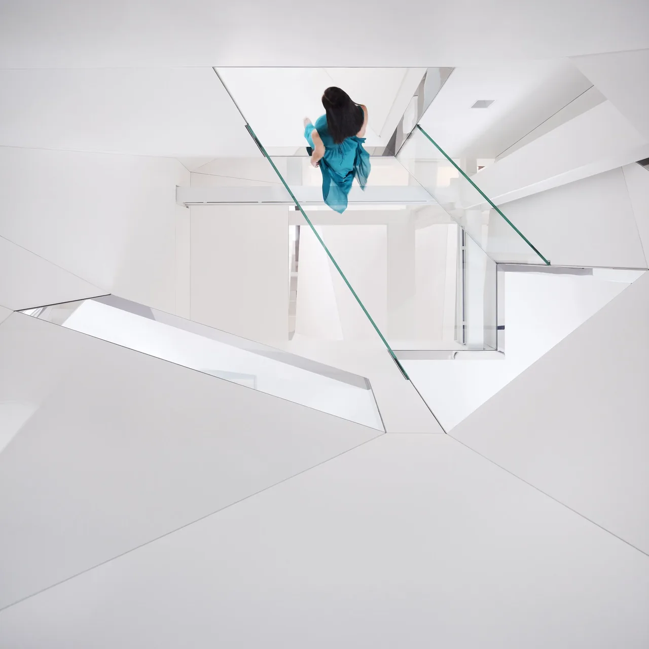 White modern stairwell features glass railings and geometric angular walls.