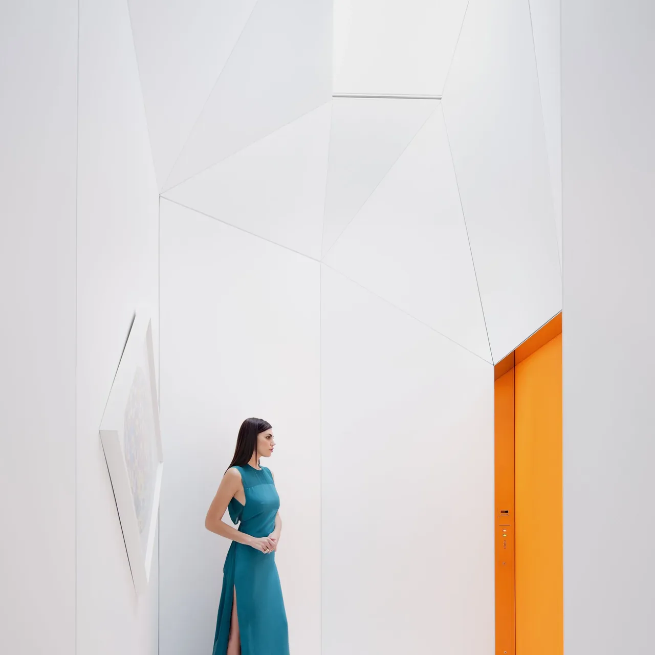 Interior of a minimalist white space with geometric wall panels and a bright orange door.