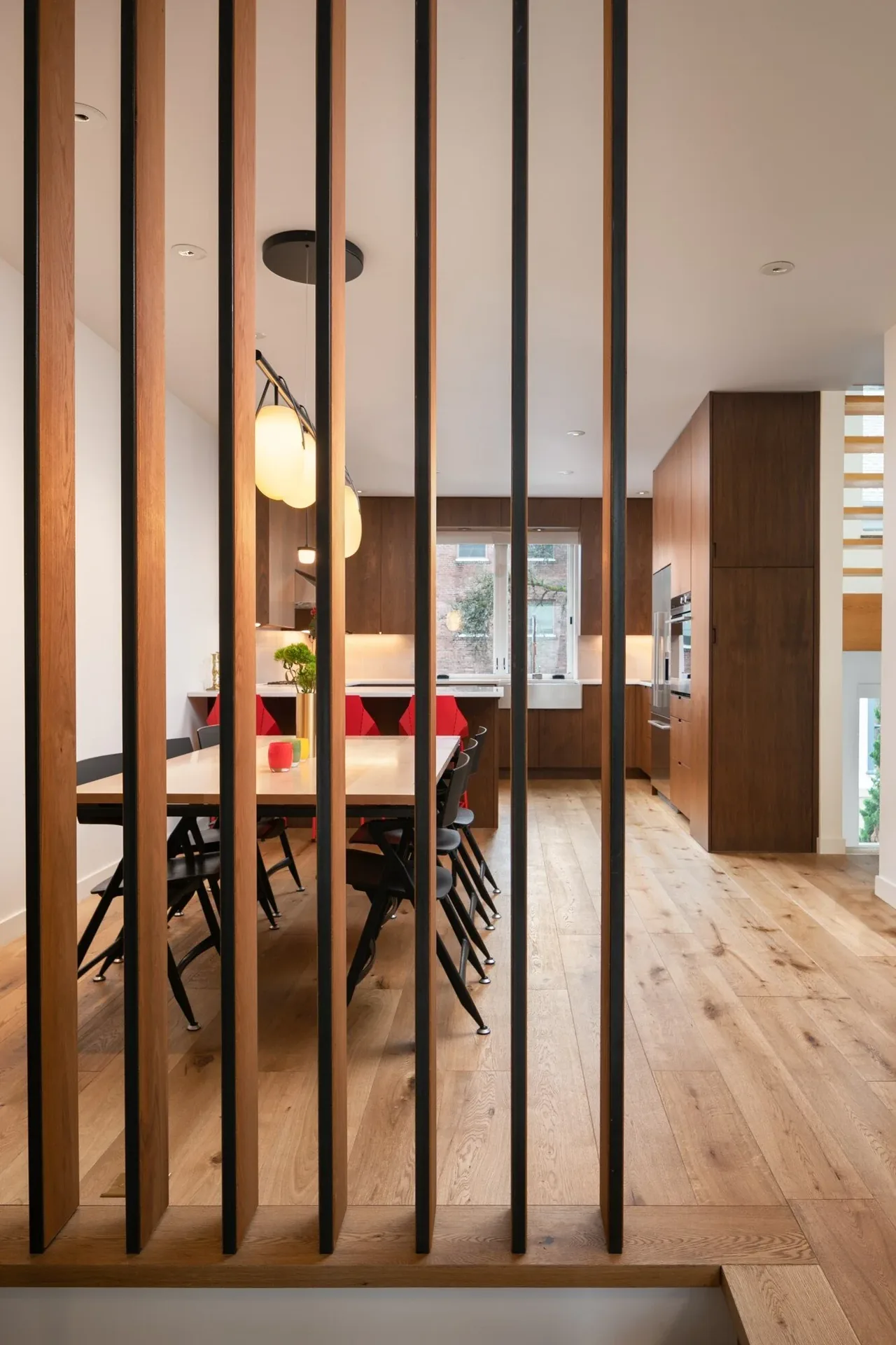 Kitchen and dining area of the E Denny Way Townhouse Renovation with wood flooring and cabinetry and vertical slat partition.