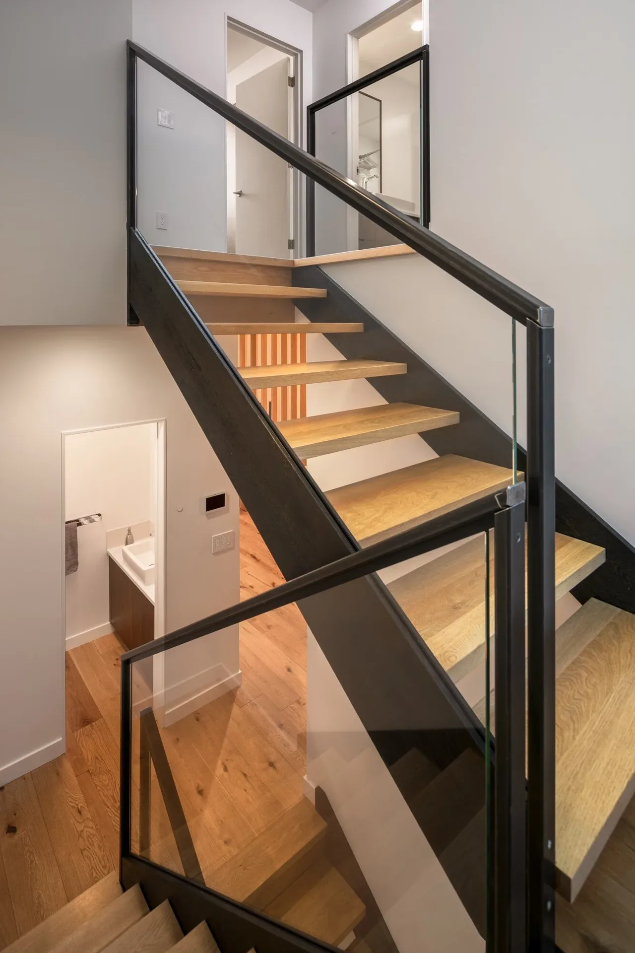 Interior stairway features open wood steps with black metal and glass railing in a modern townhouse renovation.