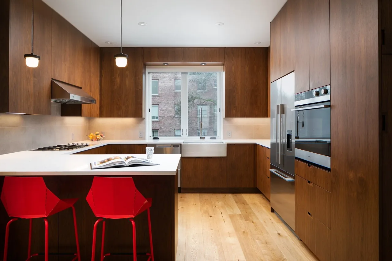 Kitchen with wood cabinets, white countertops, and two red bar stools, part of E Denny Way Townhouse Renovation in Seattle.