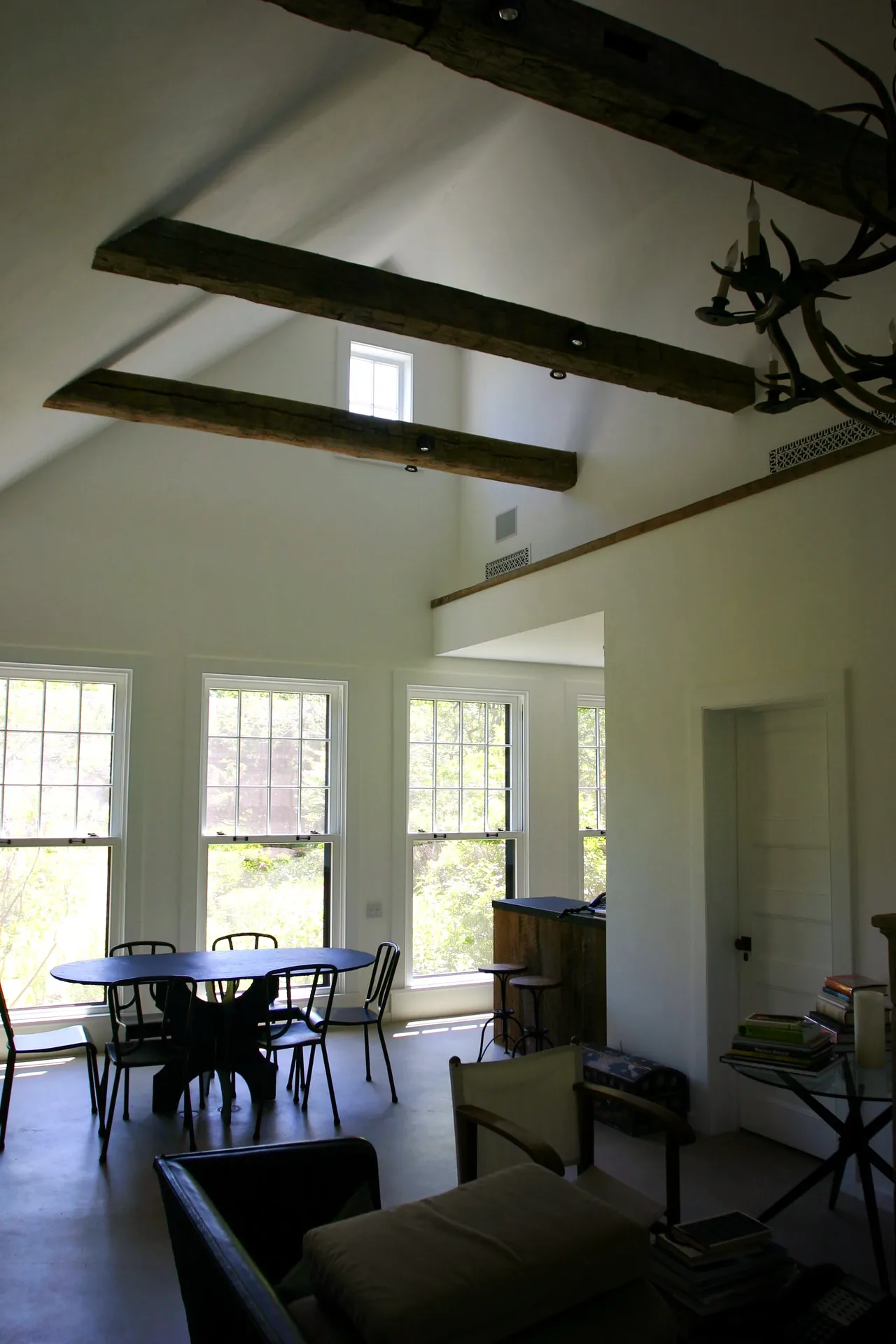 Montauk Guest Cottage features a vaulted ceiling with exposed wooden beams and large, grid-style windows in the living and dining space.
