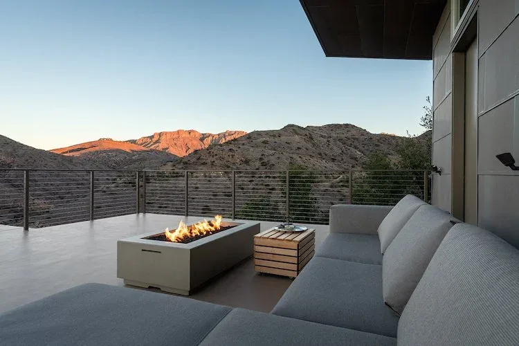 Outdoor living deck with a fire pit and seating area overlooking mountainous terrain at sunset.