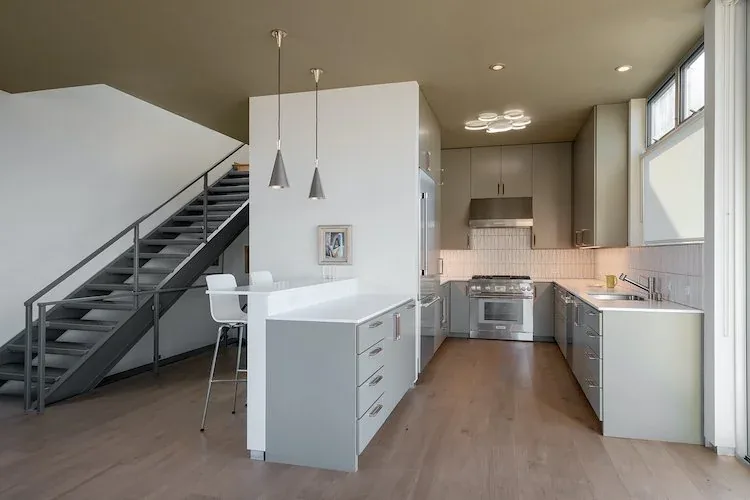 Kitchen area with gray cabinets, stainless steel gas range, and an open metal stairway adjacent to it.