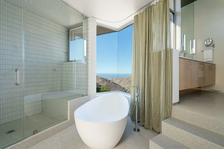 Yerba Buena Residence III bathroom features a freestanding tub, glass shower, and expansive corner window with mountain and ocean views.