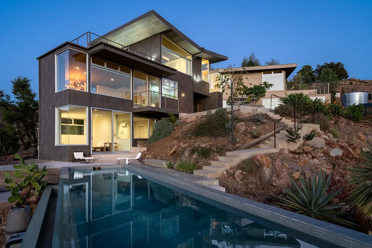 Yerba buena residence III features large glass windows, a flat roof, and a pool on a hillside site.