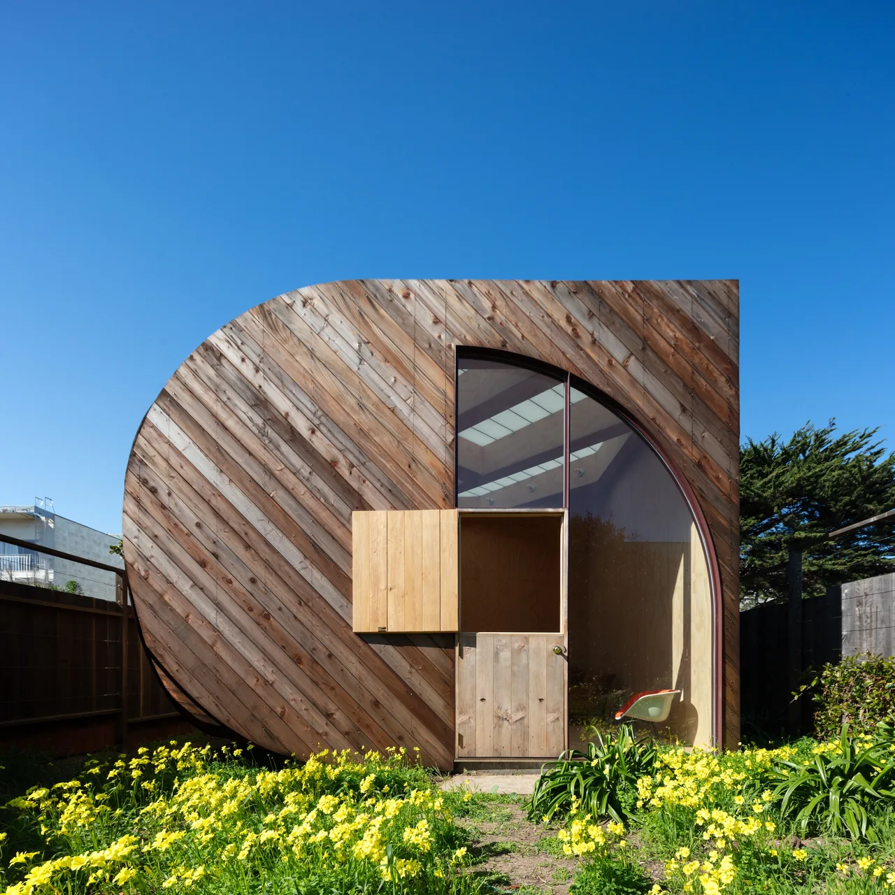 The Sandtrap features curved wood siding with a diagonal plank pattern and a tall arched window revealing interior translucent ceiling panels.