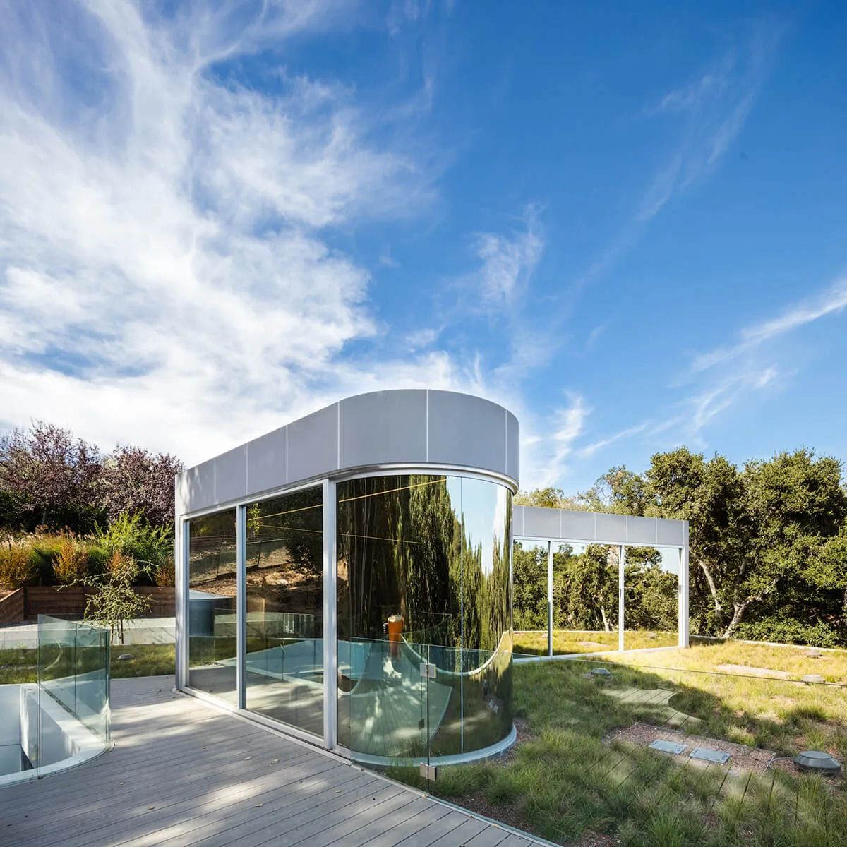 Pam & Paul's House features a curved glass corner and elevated deck with glass railing in a woodland setting in San Francisco.