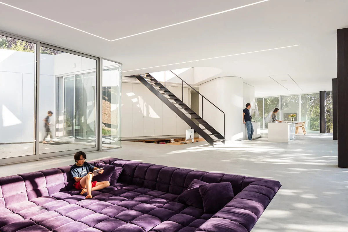 Open living area features a deep purple recessed sofa and black metal stair with natural light from floor-to-ceiling windows.