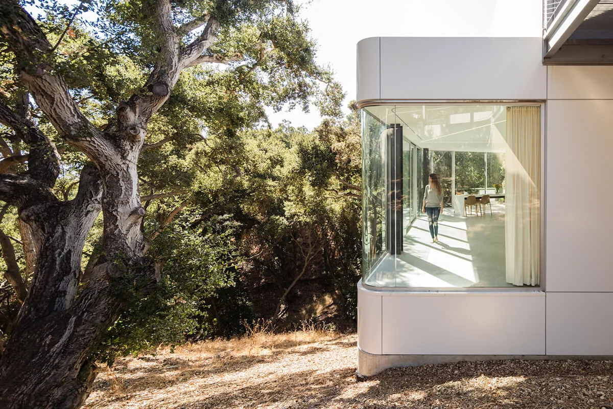 The house features a curved glass corner window that overlooks a woodland setting, bringing natural light into the interior space.
