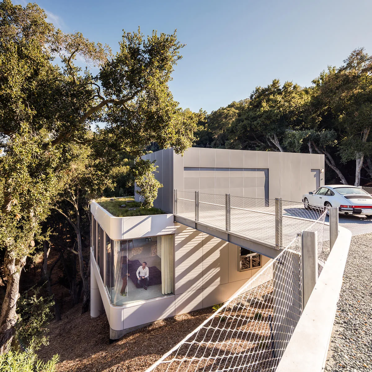 Pam & Paul’s House by Craig Steely Architecture features an elevated structure with glass railings in a woodland setting.