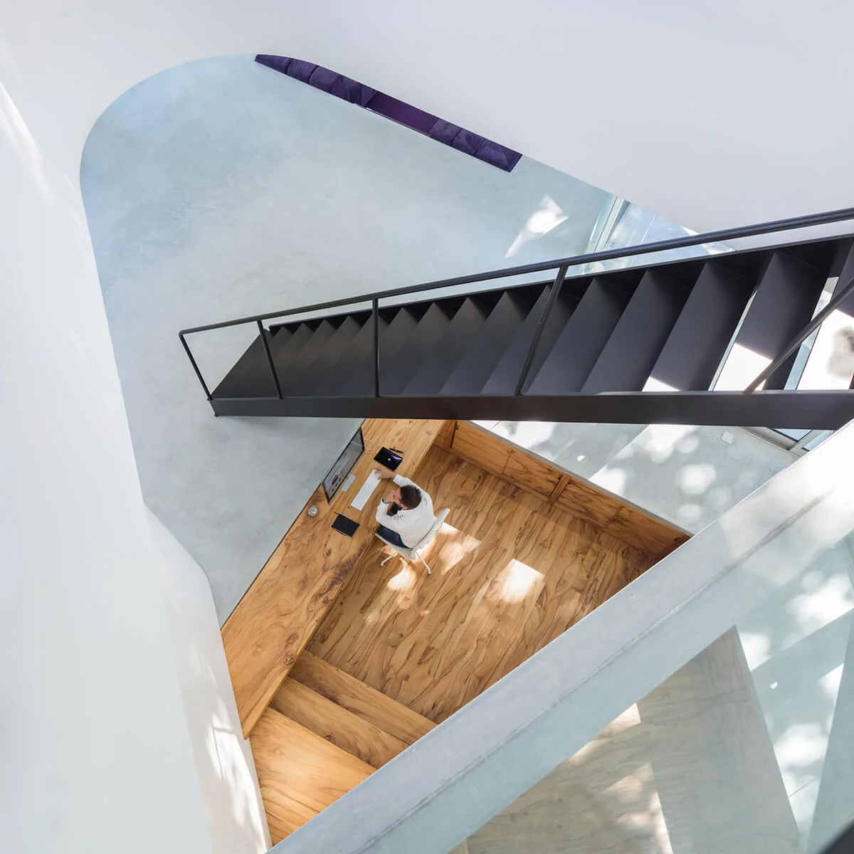 Modern black metal staircase above a sunken workspace with wood paneling and natural light.