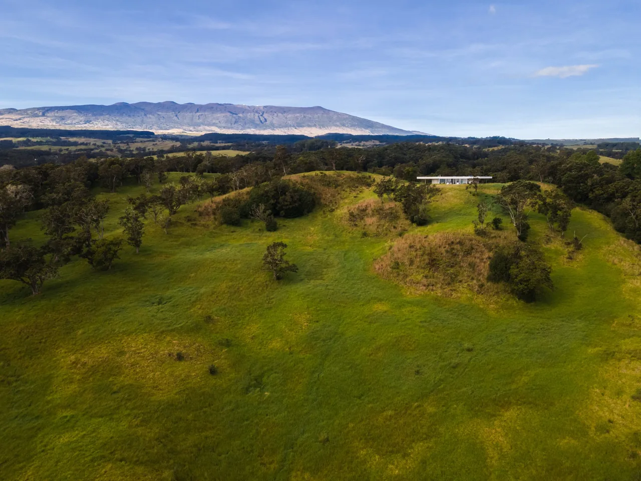 Musubi House by Craig Steely Architecture is perched on a grassy hill surrounded by natural landscape and distant mountains.
