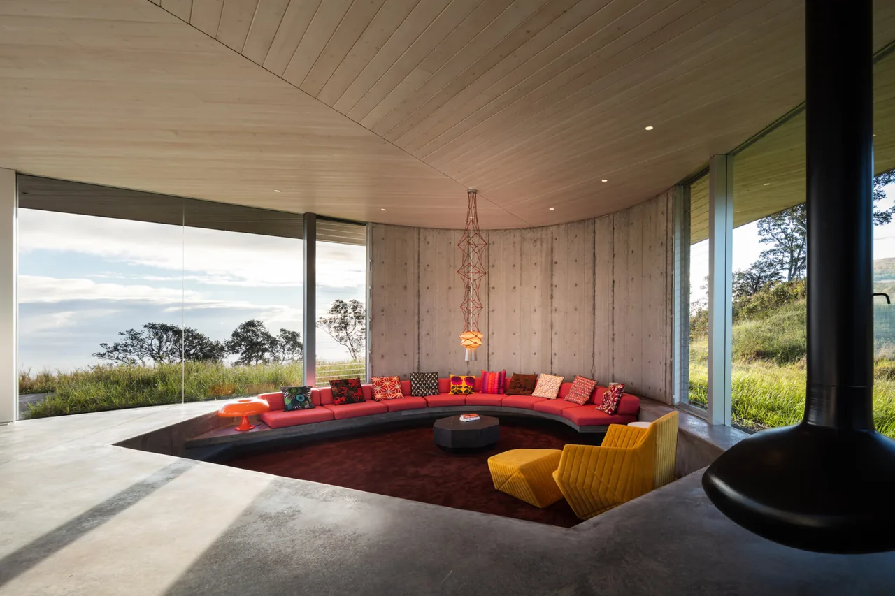 Sunken living room in Musubi House features a red sectional sofa and yellow chairs with panoramic views through floor-to-ceiling glass.