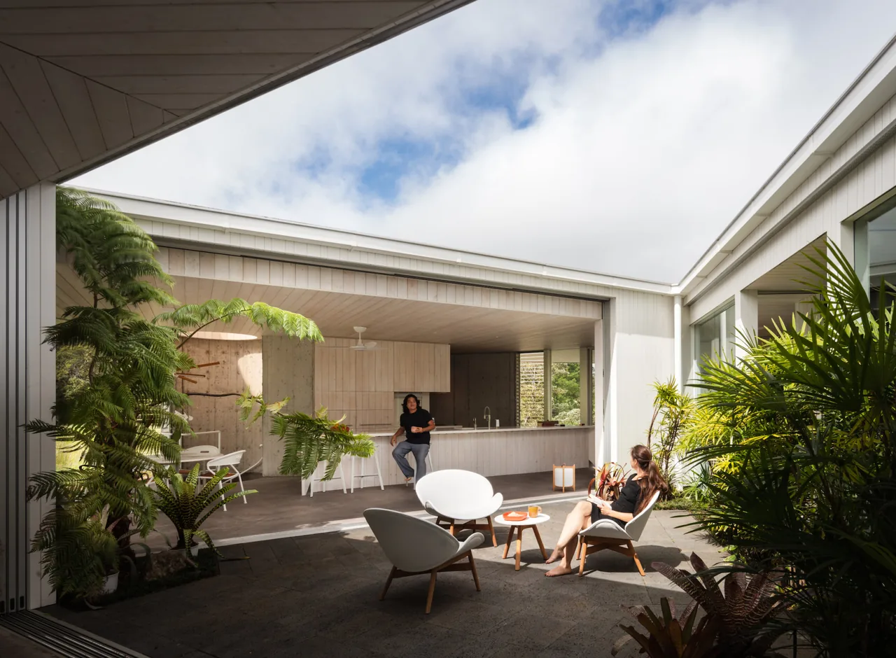 The Musubi House features a covered outdoor patio with white wood furnishings and a view into the kitchen area.