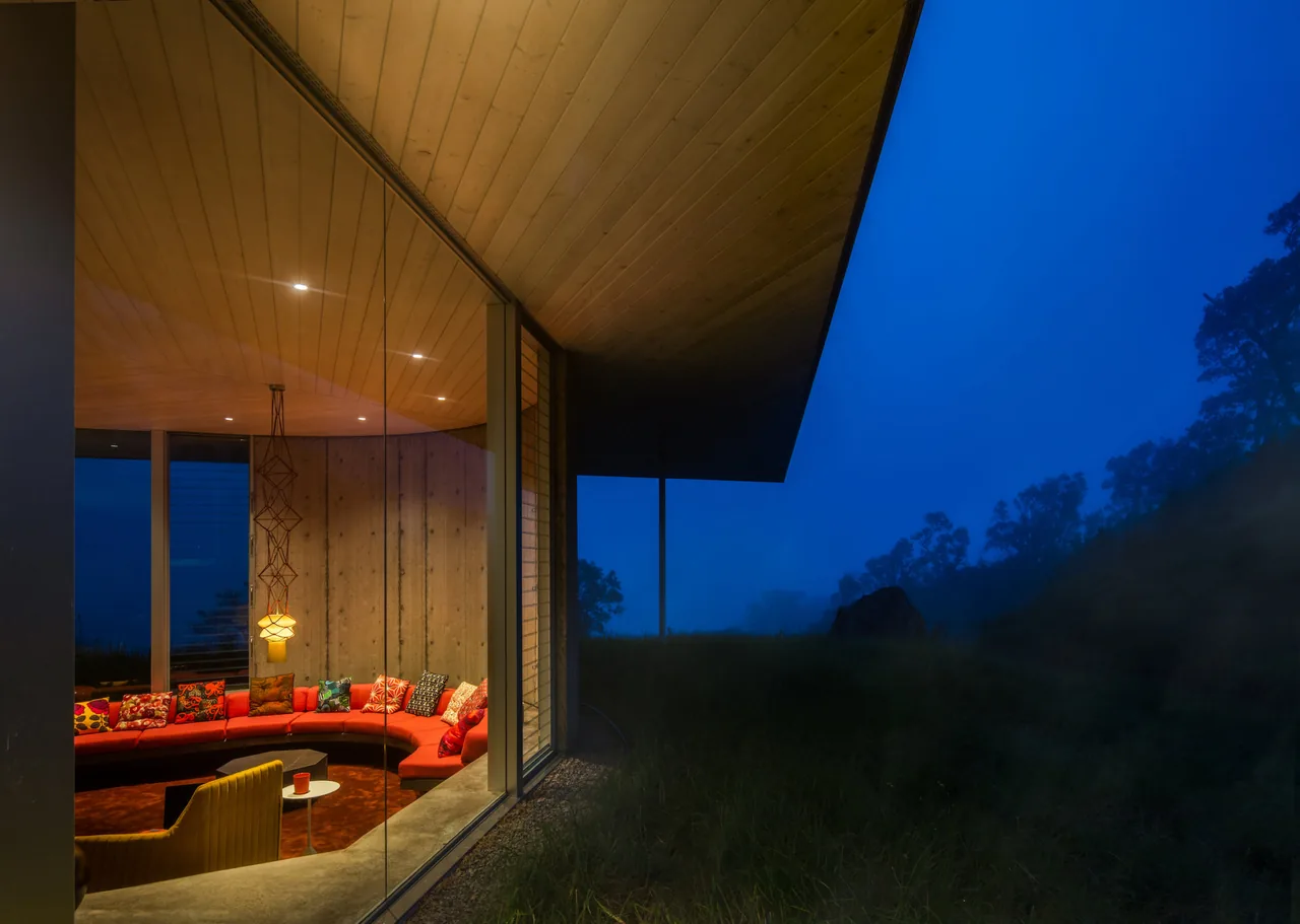 The Musubi House features a curved indoor seating area visible through floor-to-ceiling glass windows at dusk.
