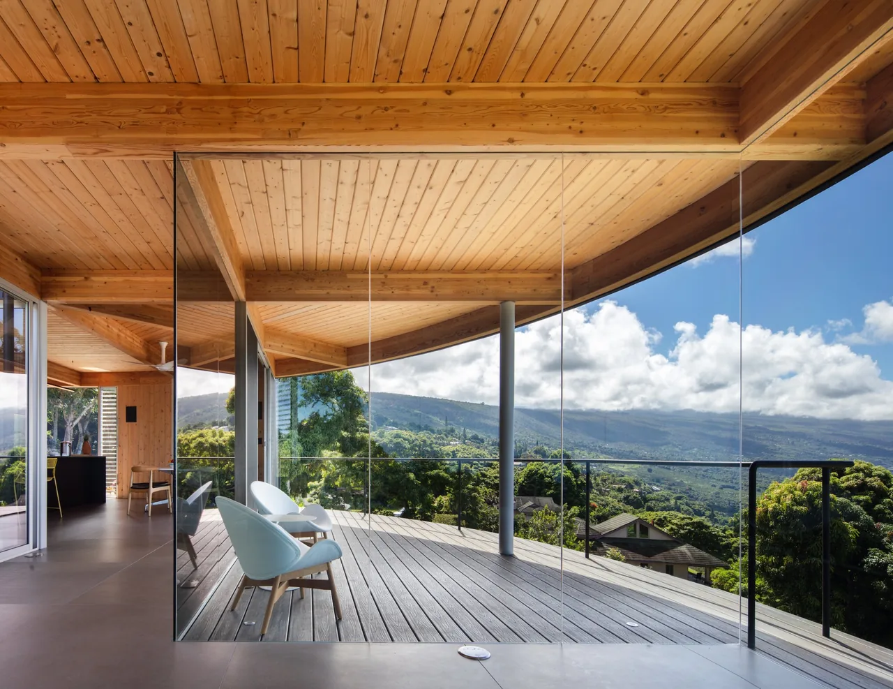 Curved outdoor deck features wood ceiling, glass railings, and views of hills and trees from D Fin House by Craig Steely Architecture.