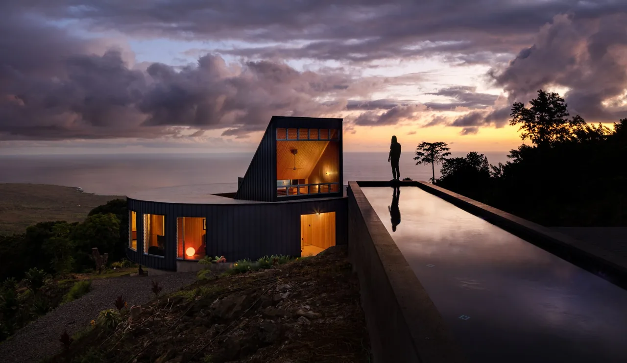 D Fin House features curved metal siding and a long reflecting pool on a hillside at sunset.