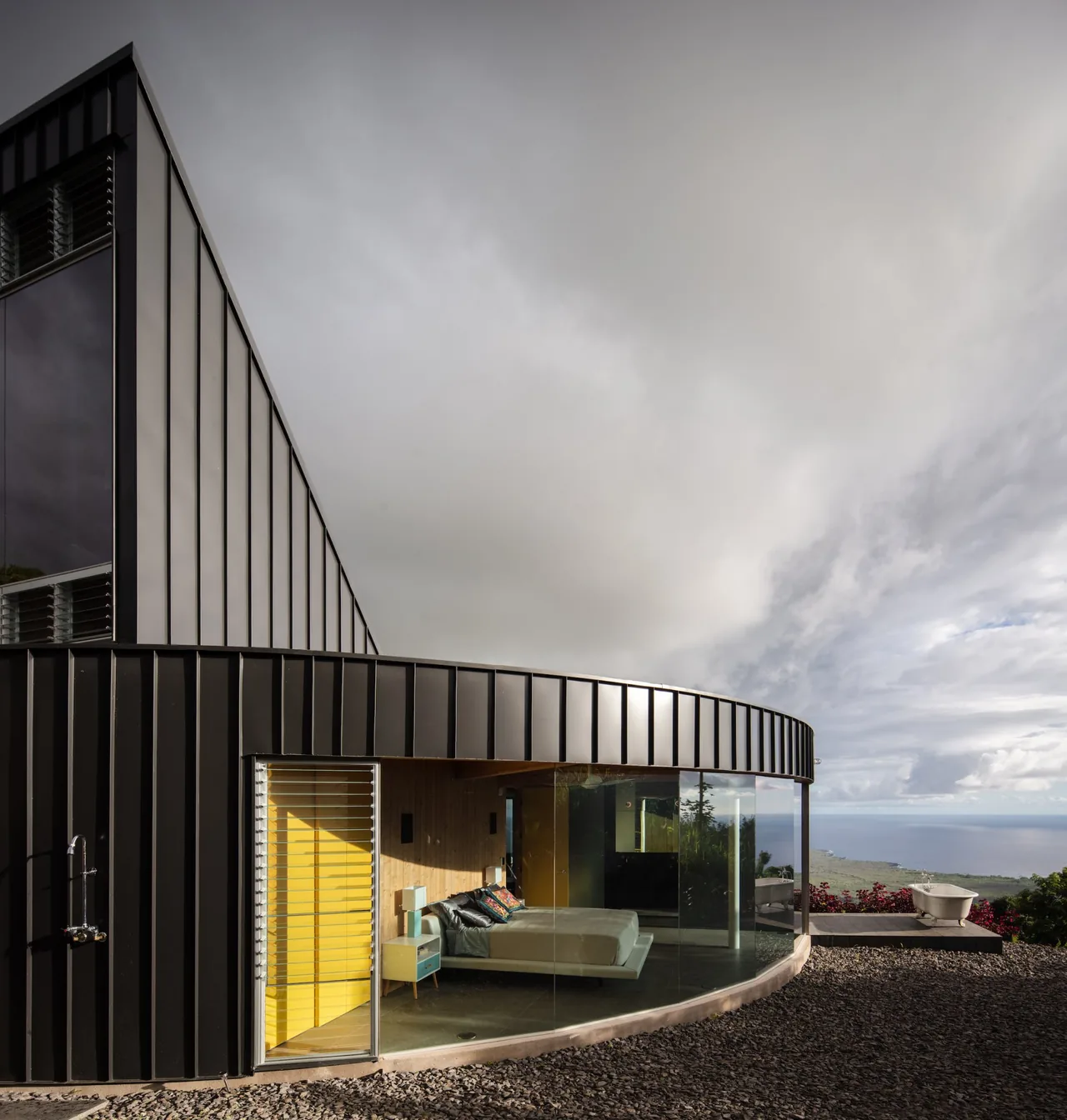 D Fin House features curved black standing seam metal exterior with floor-to-ceiling glass windows around a bedroom space