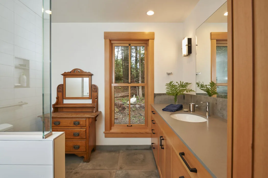 Bainbridge Island Farmhouse bathroom features wooden window trim and vanity with an oval undermount sink.