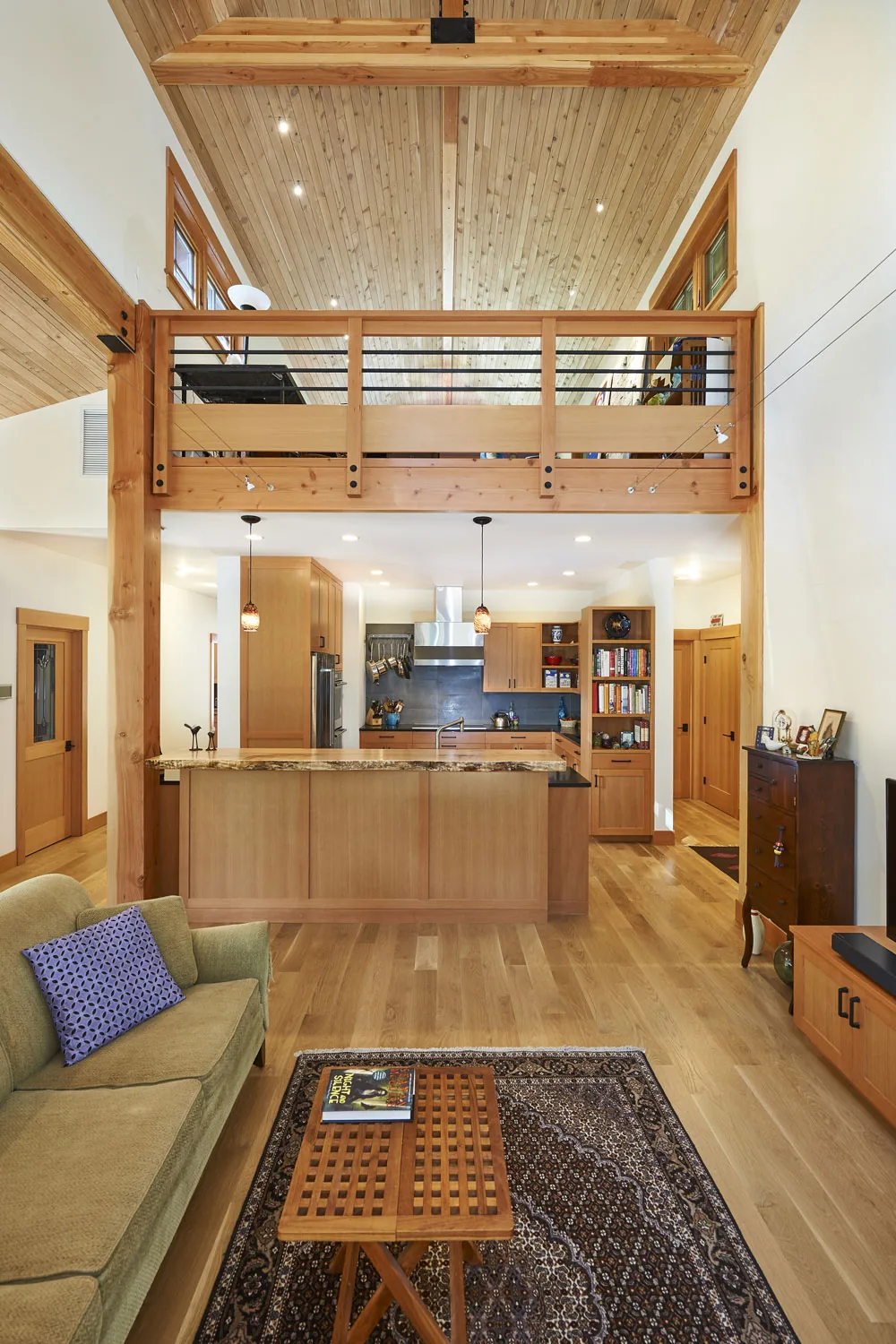 Interior featuring a wood-paneled vaulted ceiling, kitchen with wood cabinets, and a cable railing mezzanine above the kitchen island.