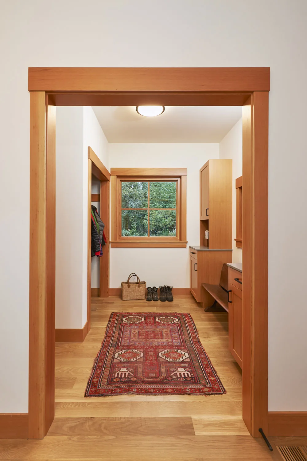 Mudroom with wood window trim, natural wood cabinetry, and a red decorative rug on oak flooring.