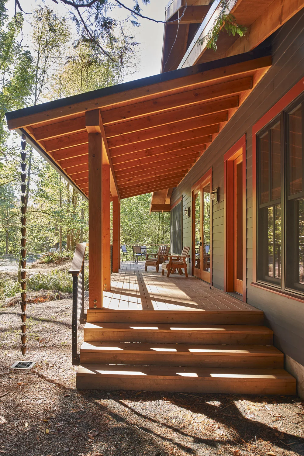 Covered wooden porch with exposed beams and steps at the Bainbridge Island Farmhouse by CTA Design Builders.