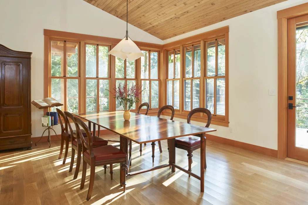 Dining area with wood framed windows and vaulted ceiling in Bainbridge Island Farmhouse project by CTA Design Builders.