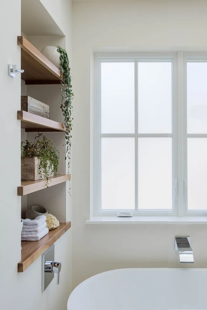Bathroom with a freestanding tub beneath a window with divided lites and wood shelves with plants and towels.