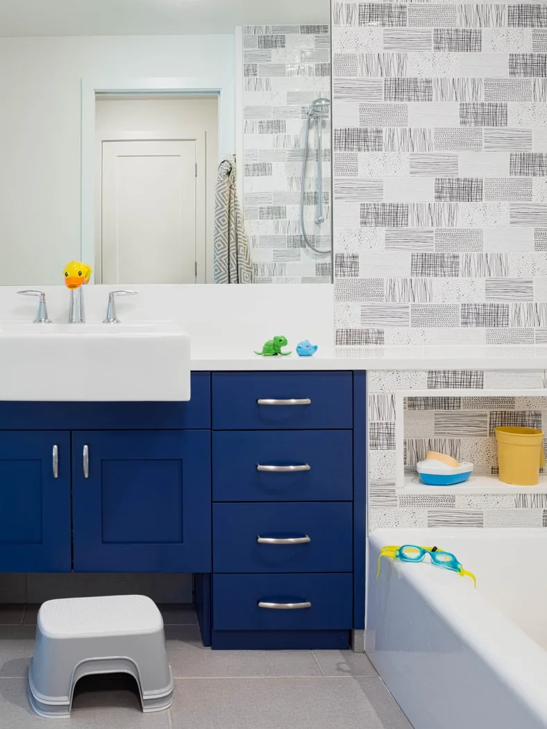 Bathroom features blue lower cabinets, abstract patterned tile, and a white countertop with a built-in sink.