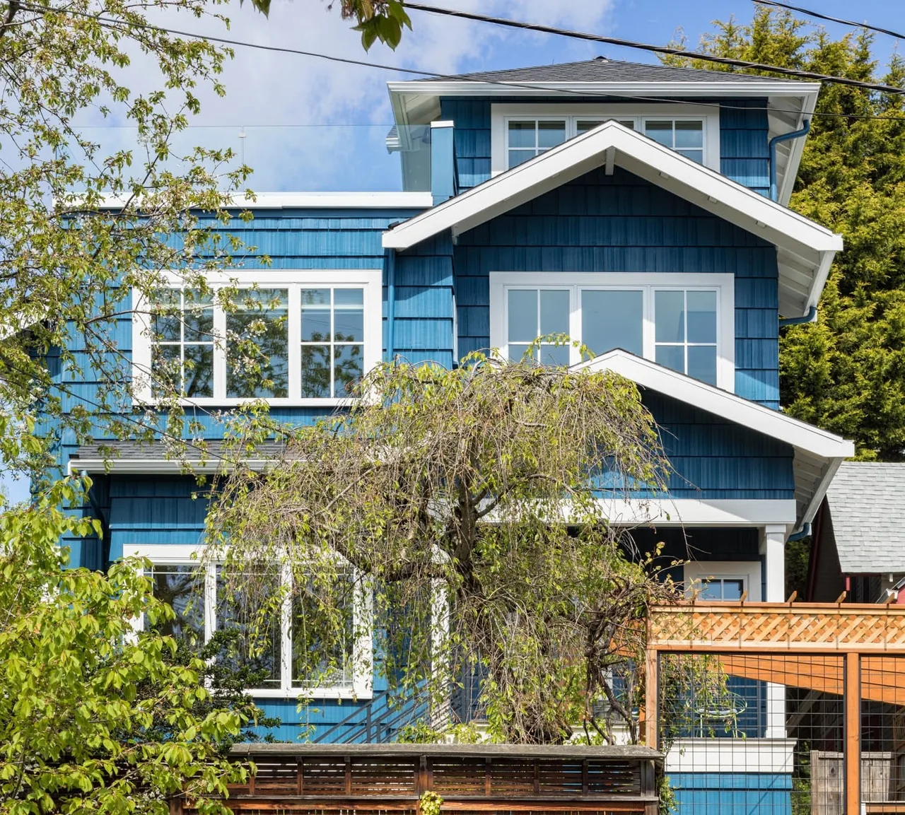 Front view of a blue urban farmhouse with white trim and multiple gable roofs designed by CTA Design Builders in Seattle.