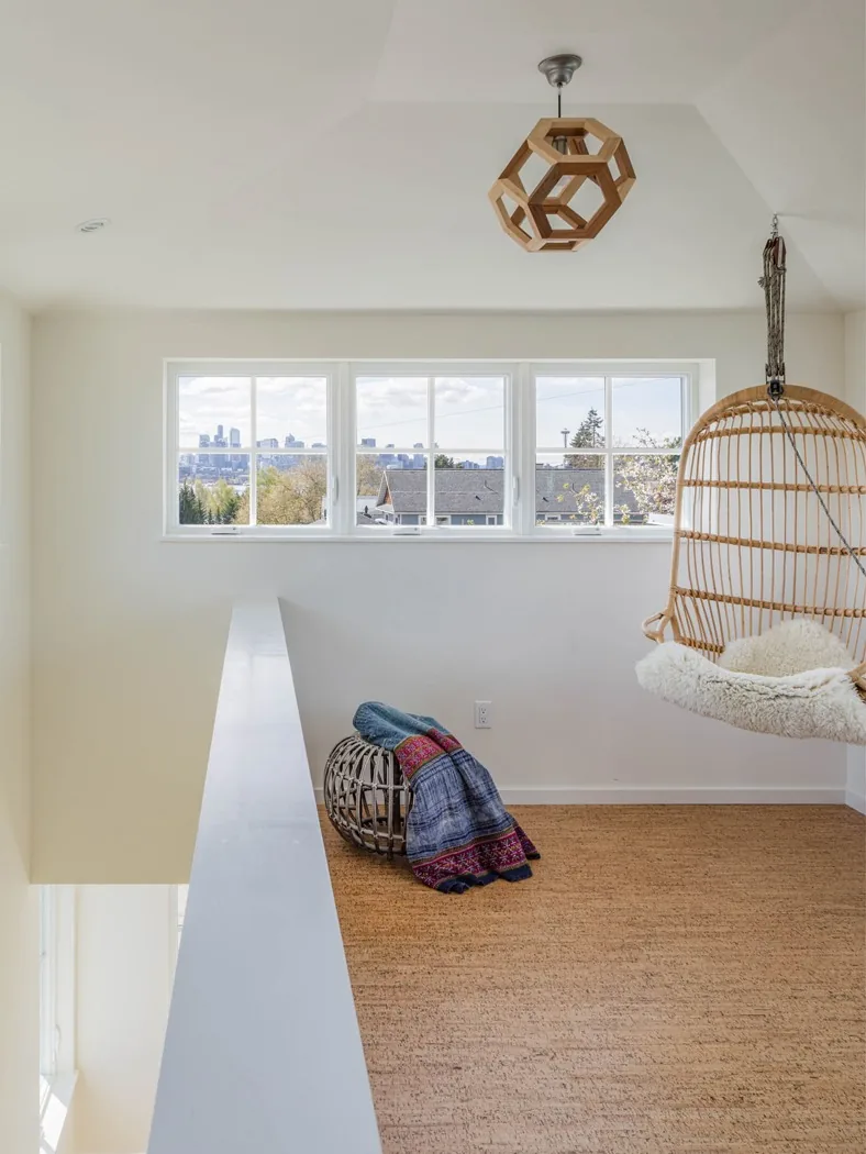 Landing with window views of city skyline, suspended rattan chair, and geometric ceiling light fixture.