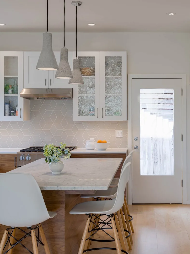 The Urban Farmhouse kitchen features white cabinetry with glass doors, a hexagonal tile backsplash, and a marble island countertop with pendant lighting.